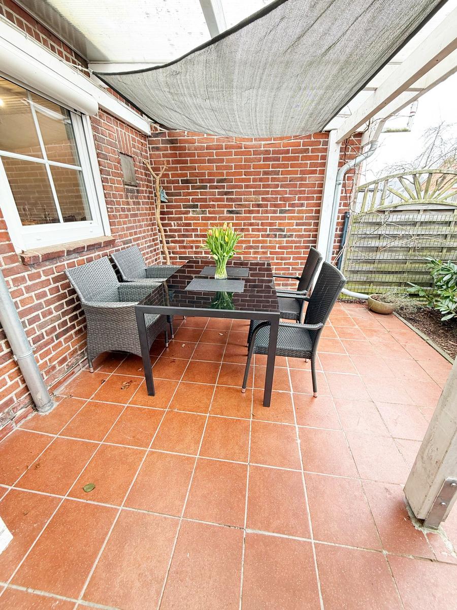 Terrasse mit Tisch, vier Stühlen und Sonnensegel. Terrakottafußboden und Backsteinwand.