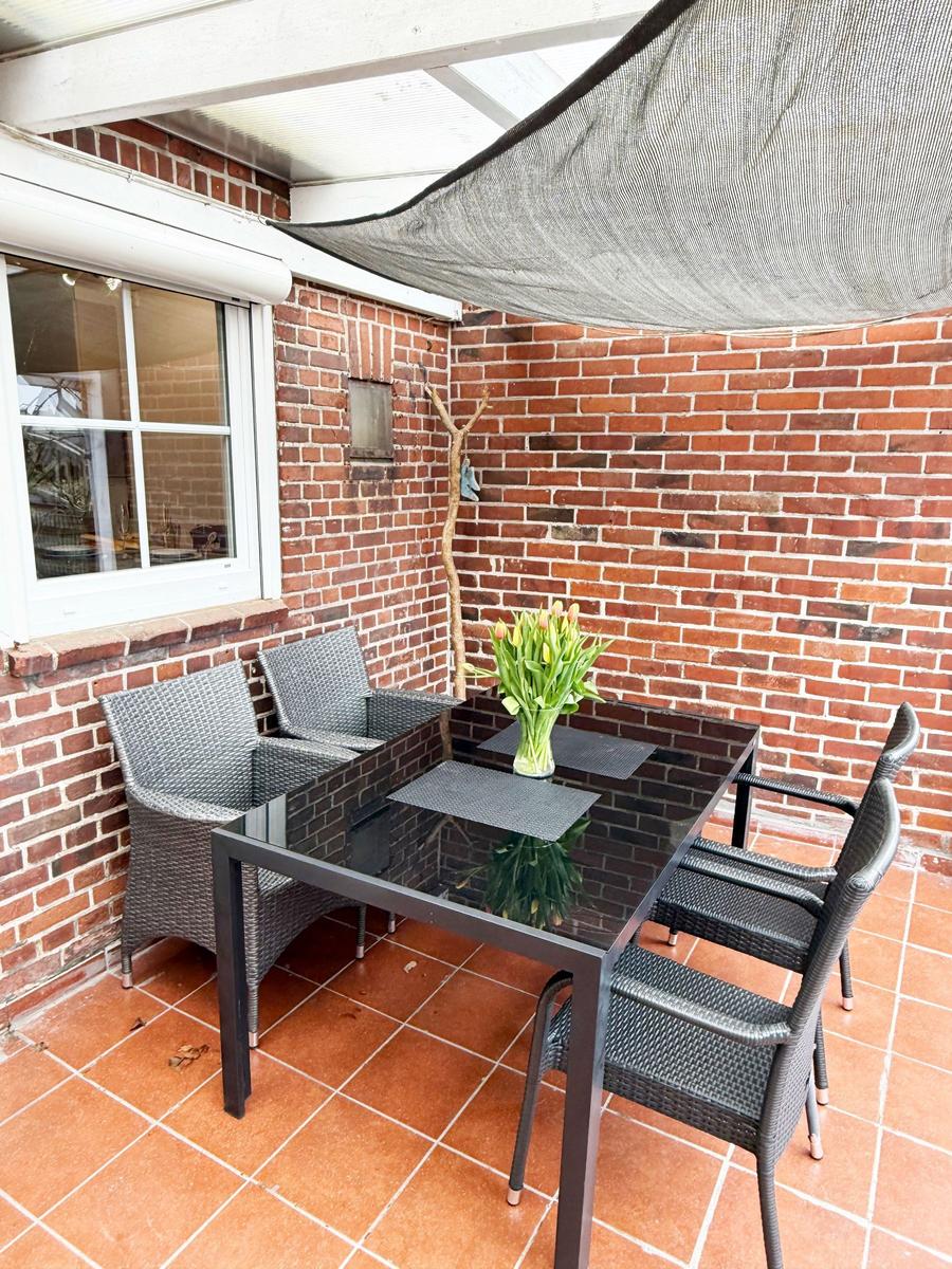 Terrasse mit Tisch, Stühlen und Blumen vor Backsteinwand unter Sonnenschutz