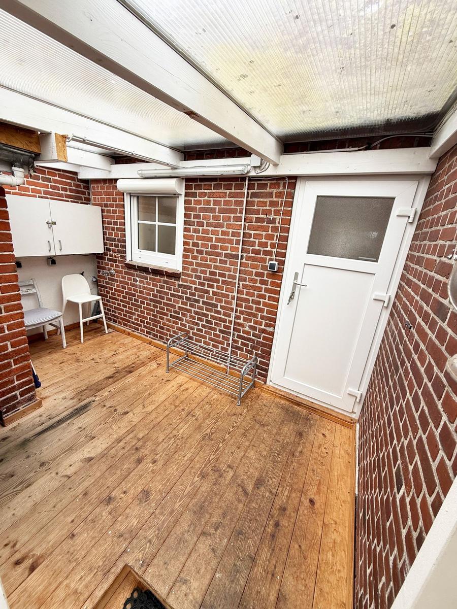 Räumlichkeiten mit Holzboden, Backsteinwänden und weißer Tür. Ein Fenster und ein kleiner Schrank sind sichtbar.