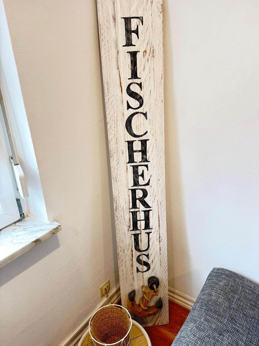 Hölzernes Schild mit der Aufschrift FISCHERHUS an der Wand neben einem Fenster.