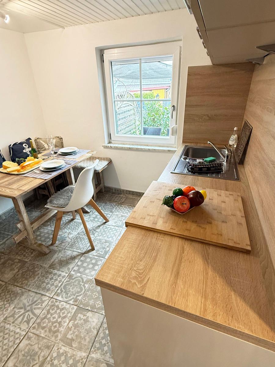 Küche mit Essbereich, Holztisch, Fenster und Obst auf der Arbeitsfläche.