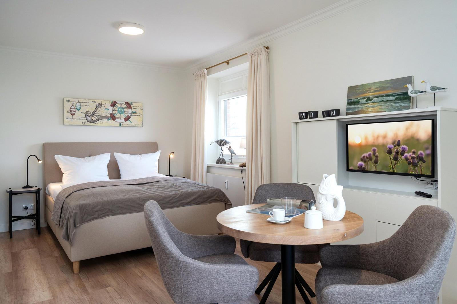 Schlafzimmer mit Bett, Esstisch und Fernseher. Wandbild und Fenster mit Vorhängen.