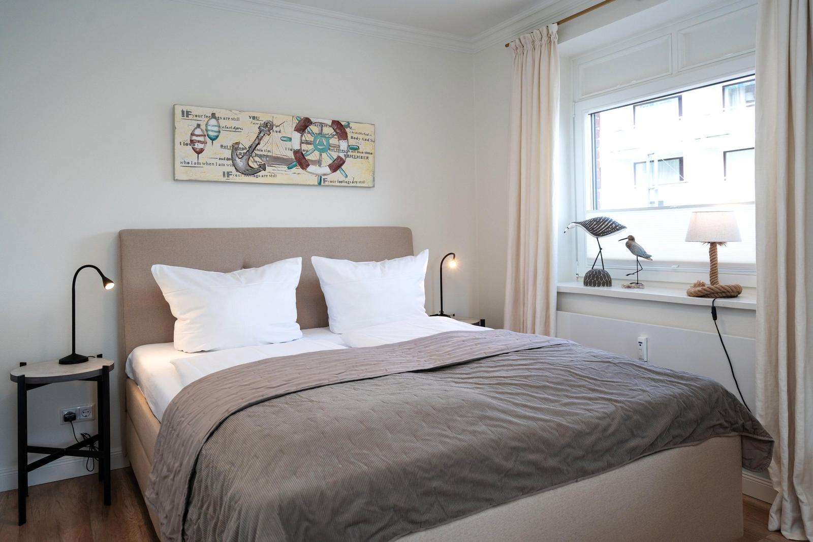 Schlafzimmer mit Bett, Nachttisch und Fenster mit Vorhängen.