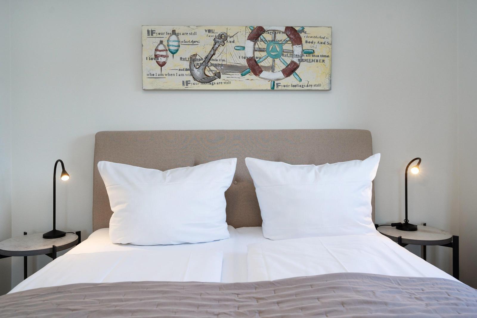 Schlafzimmer mit Bett, zwei Nachttischen und Wandbild mit Seemannsmotiven.