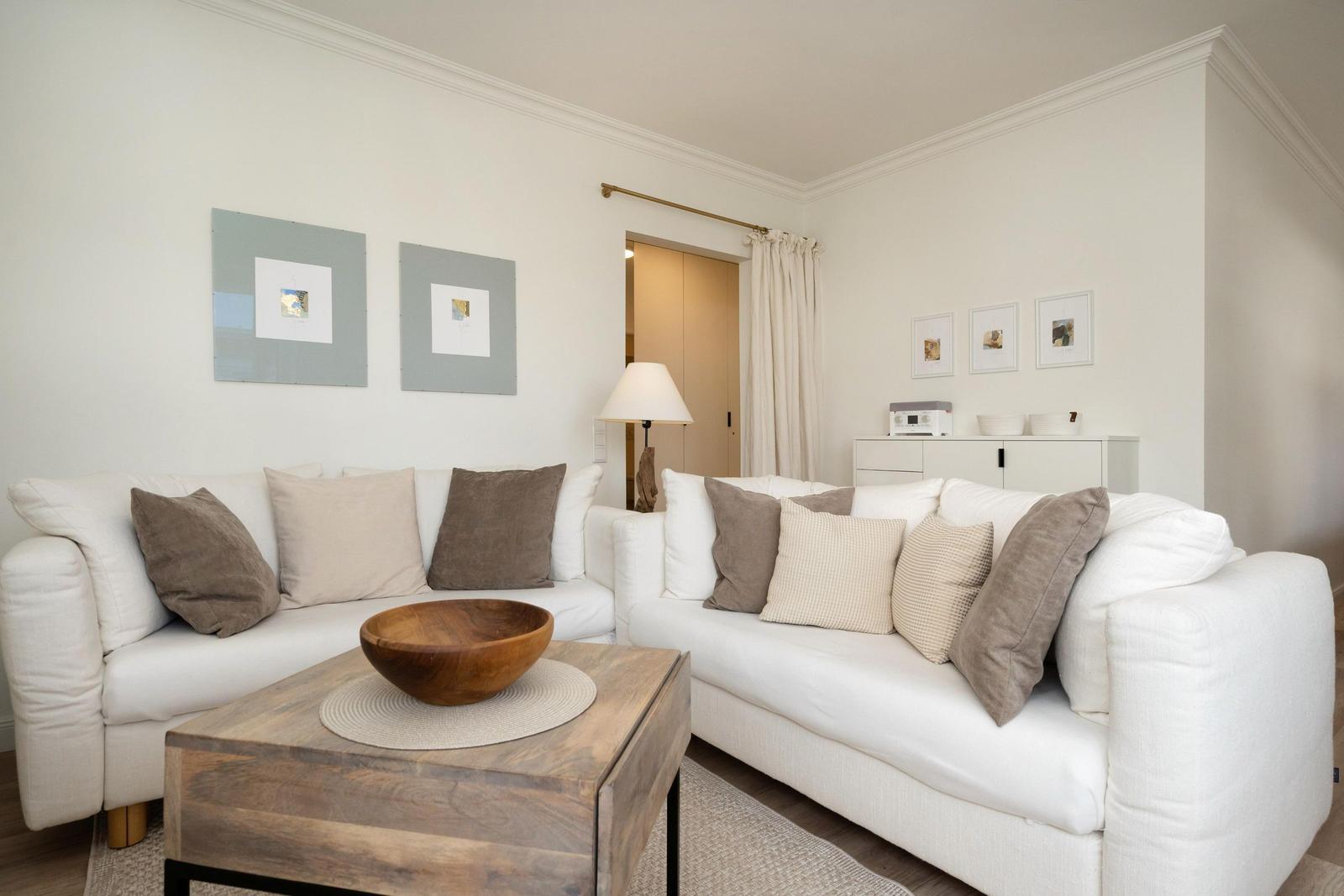 Wohnzimmer mit weißen Sofas, Holztisch und Wandbildern.