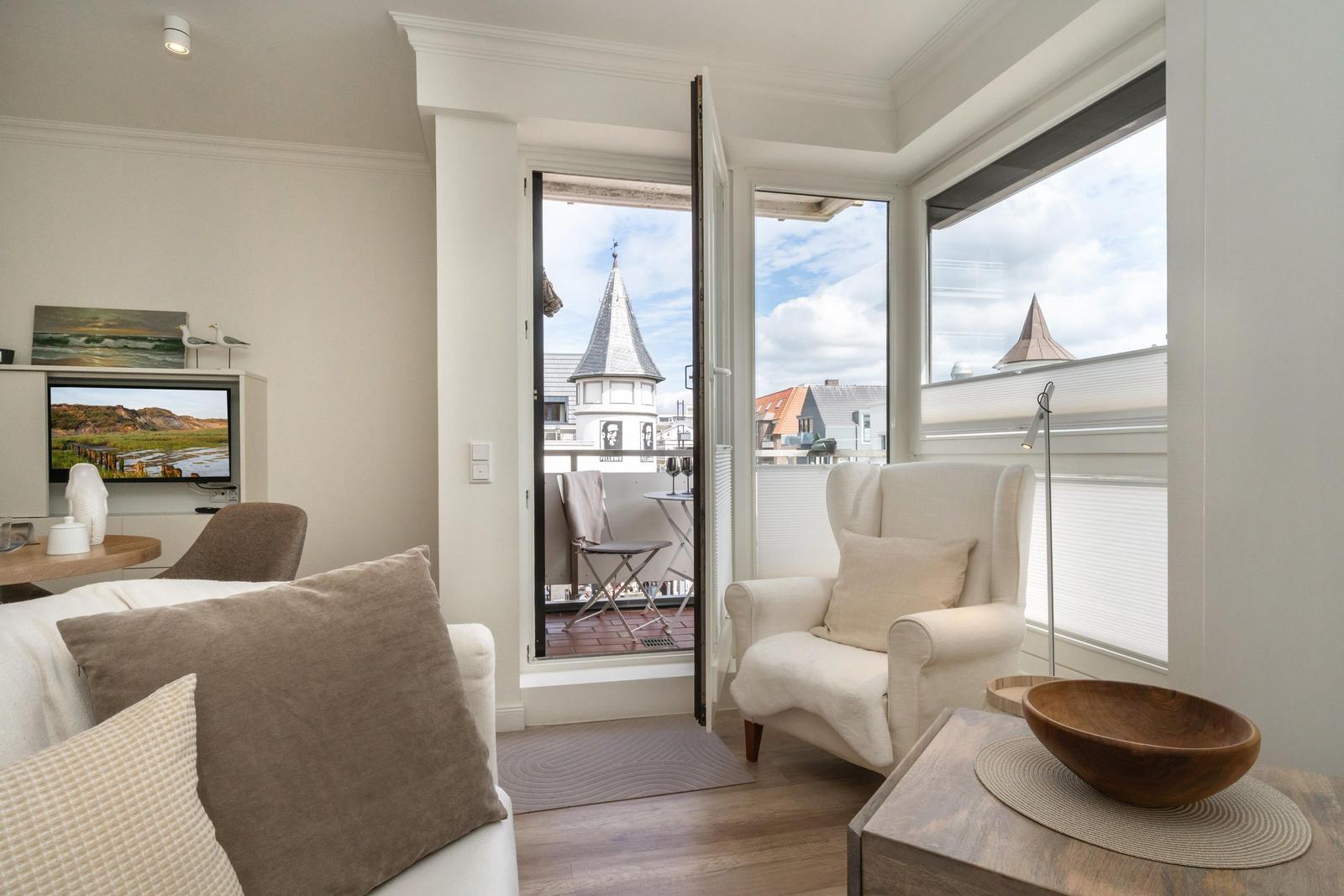 Wohnzimmer mit Blick auf Turm und Balkon. Fernseher, Sessel und Holztisch.