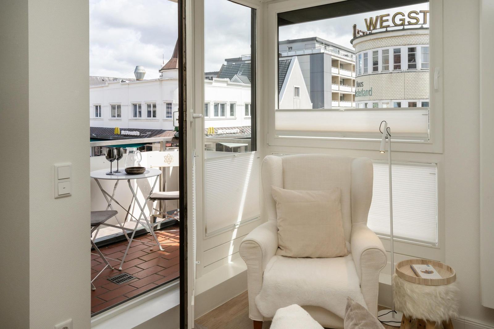 Ein Raum mit Sessel, Tisch und Blick auf Balkon und Stadt.