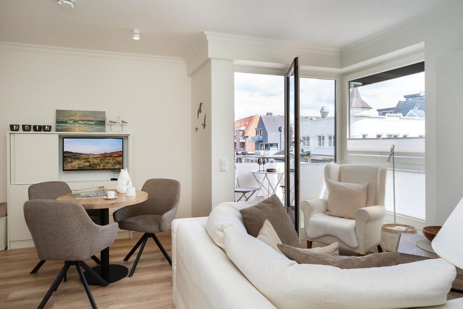 Wohnzimmer mit Sofa, Esstisch und Balkonansicht. Fernseher und Dekoration sichtbar.
