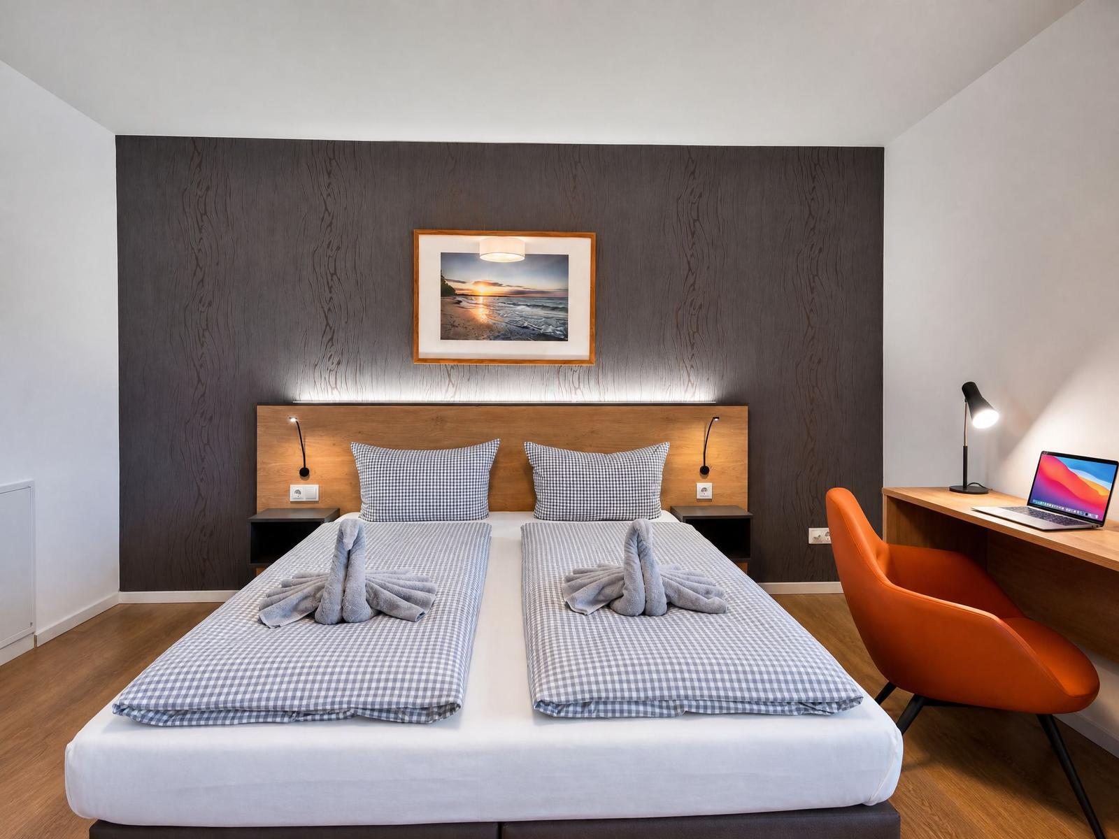 Zweibettzimmer mit Holzwand, Schreibtisch und orangefarbener Sitzgelegenheit.