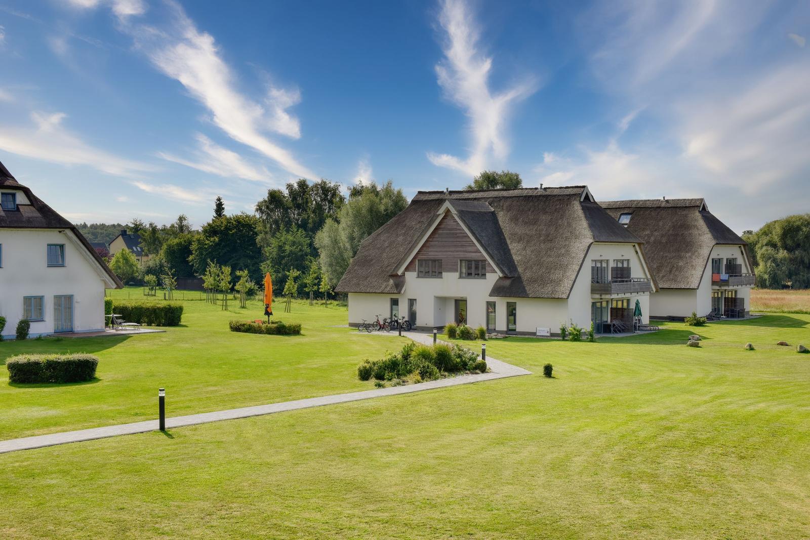 Haus mit Strohdach, großer Grünfläche und Terrassen. Fahrräder und Sonnenschirm sind vorhanden.
