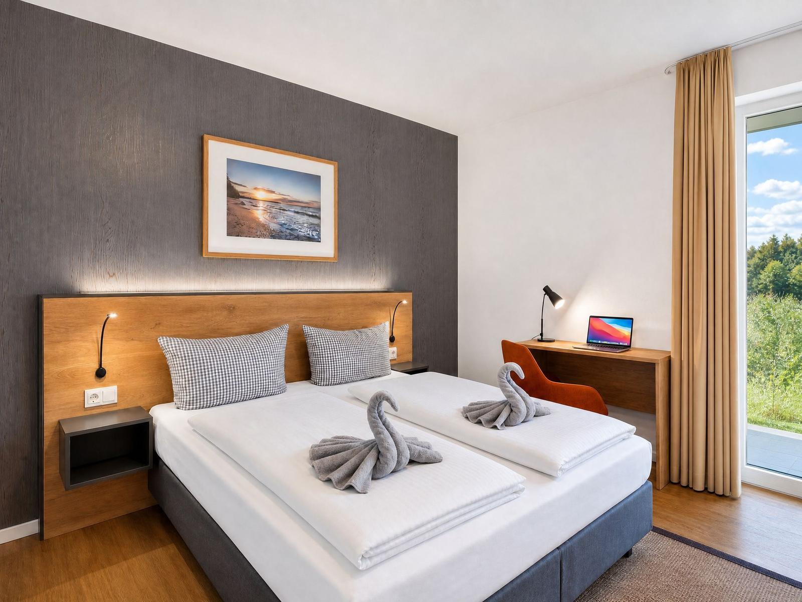 Zimmer mit Doppelbett, Schreibtisch und Blick auf Grünflächen.