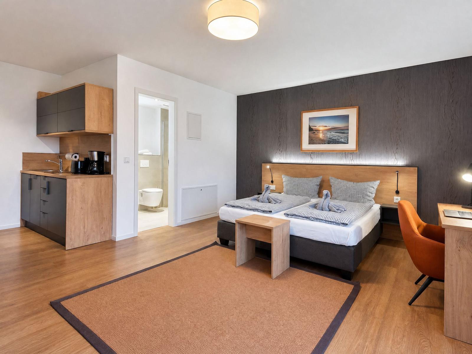 Schlafzimmer mit Doppelbett, Schreibtisch, Küchenzeile und Bad