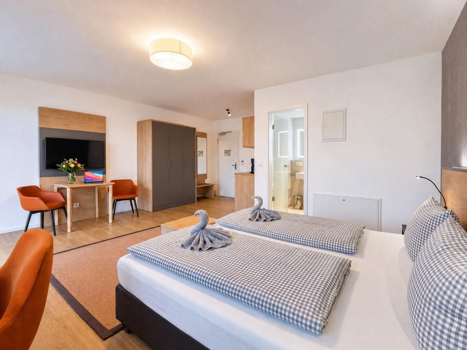 Zimmer mit Doppelbett, Schreibtisch, TV und Bad. Handtuchschwanen auf dem Bett.