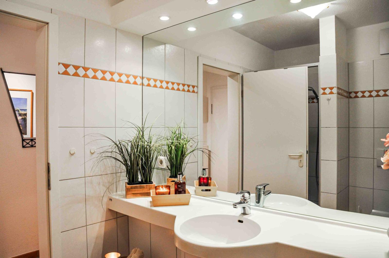 Badezimmer mit Waschbecken, Spiegel und Dusche. Wandfliesen mit orangefarbenem Muster.