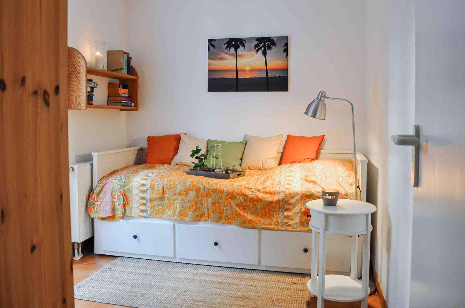 Schlafzimmer mit Bett, Kissen und Wandbild. Neben dem Bett steht ein Nachttisch.