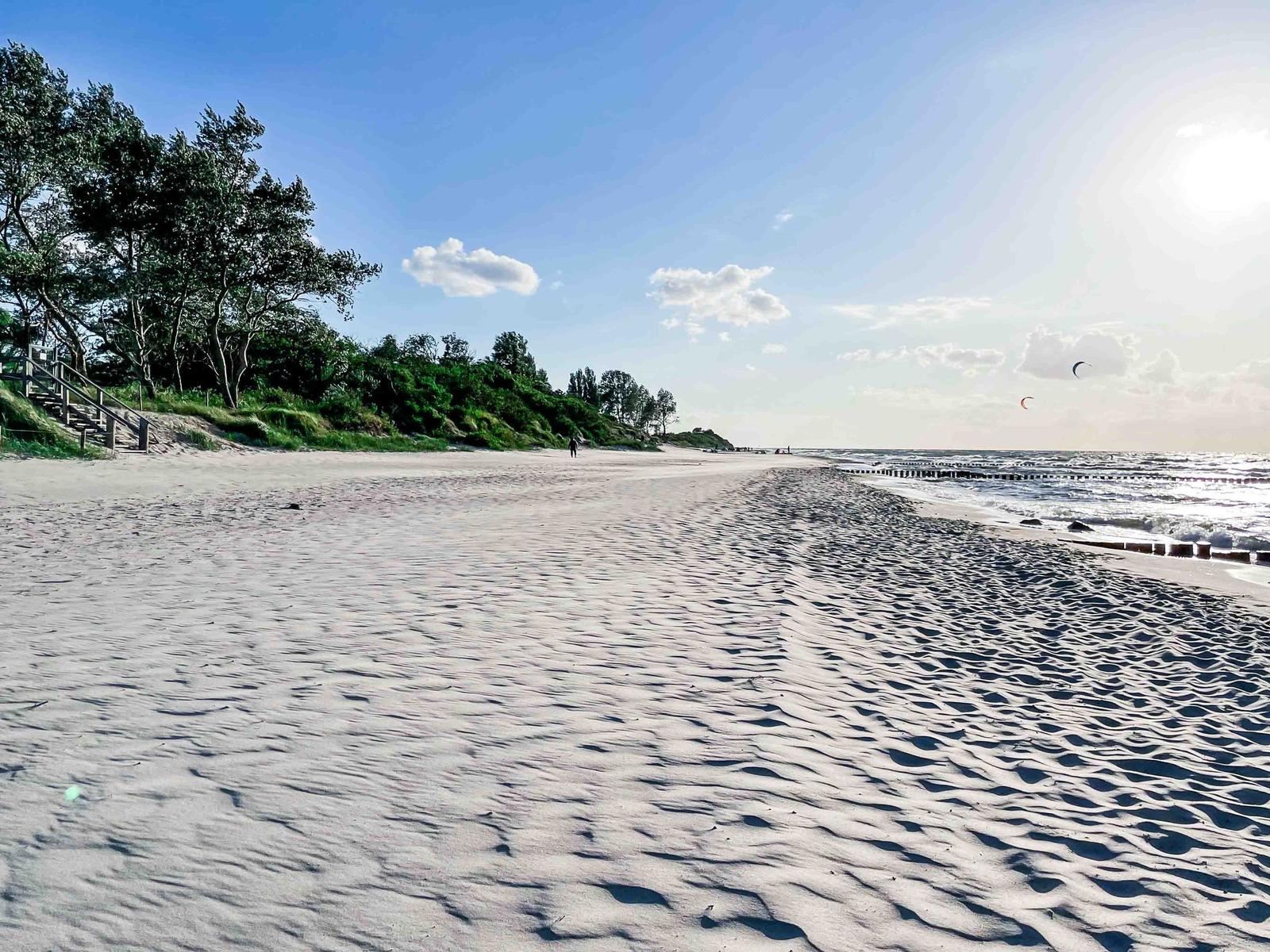 Weiterer Sandstrand mit Bäumen und Kitesurfern am Horizont.