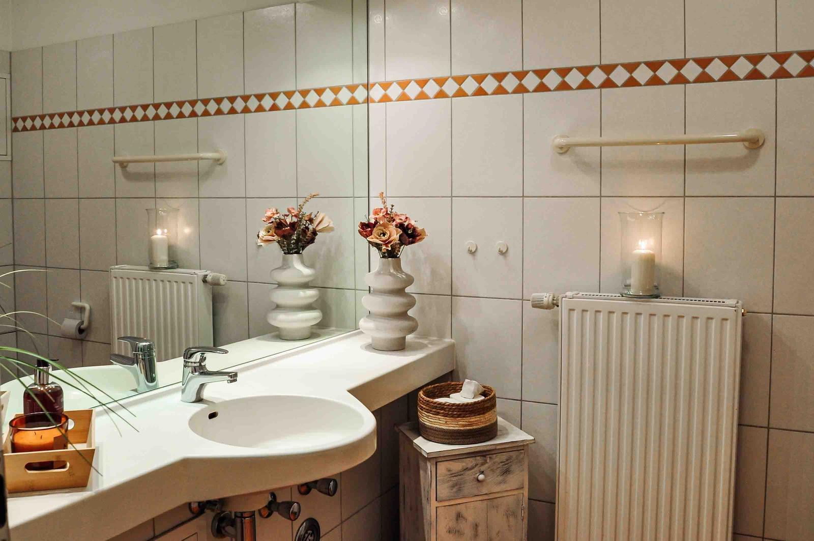 Badezimmer mit Waschbecken, Spiegel, Heizkörper und Vasen mit Blumen.