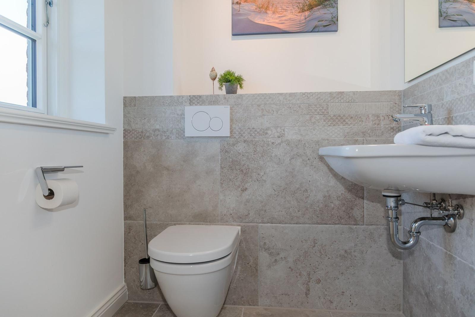 Bathroom with toilet, sink, and window. Wall cladding made of stone tiles.
