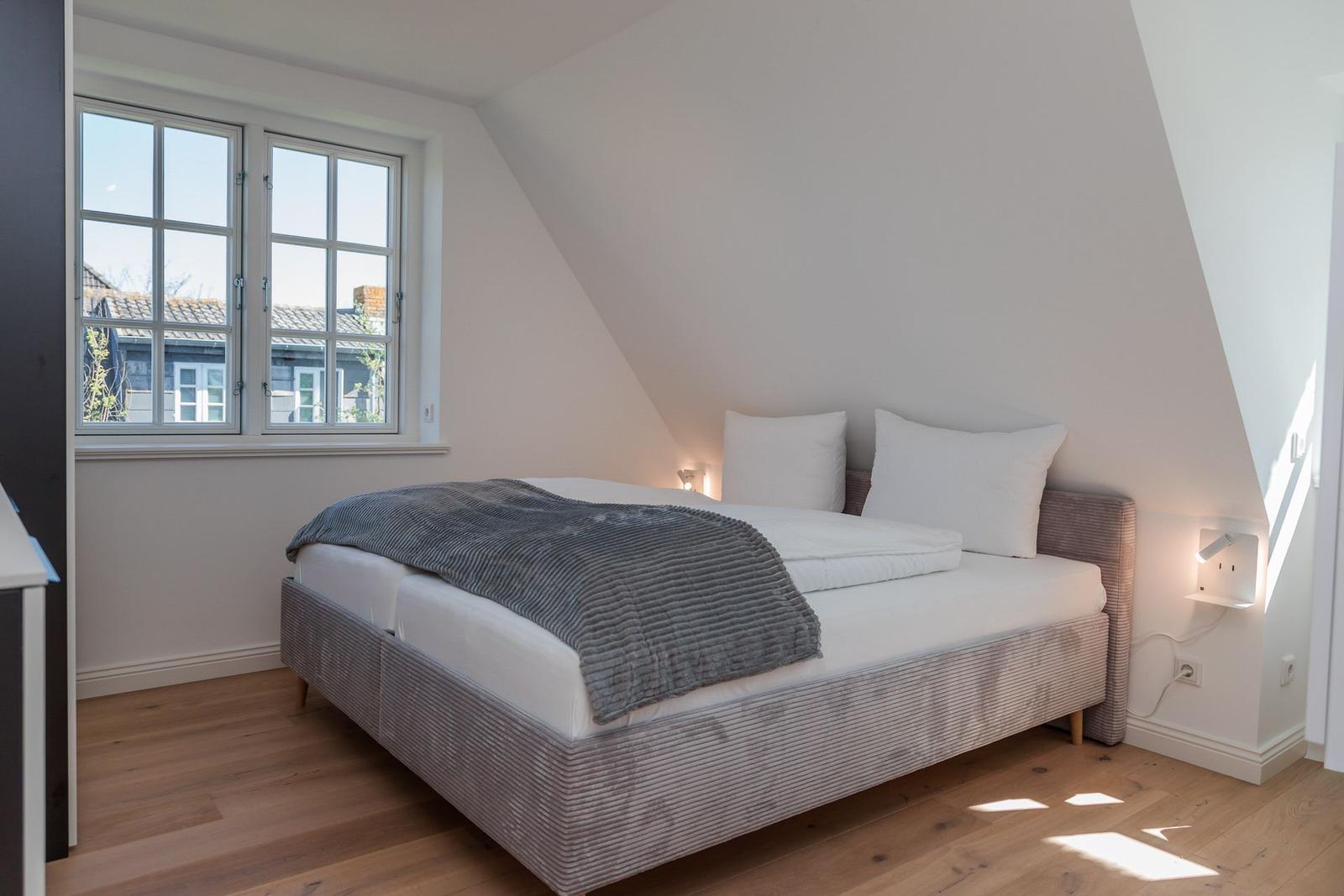Bedroom with sloped ceiling, large window, and bed with gray blanket.