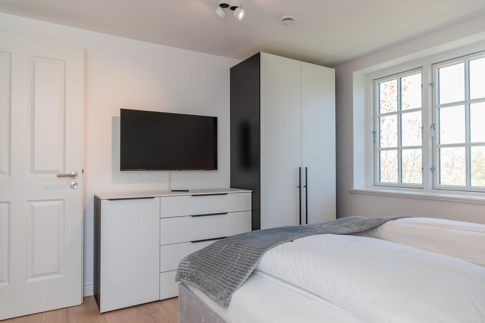 Bedroom with bed, TV, and wardrobe. Window with view of trees.