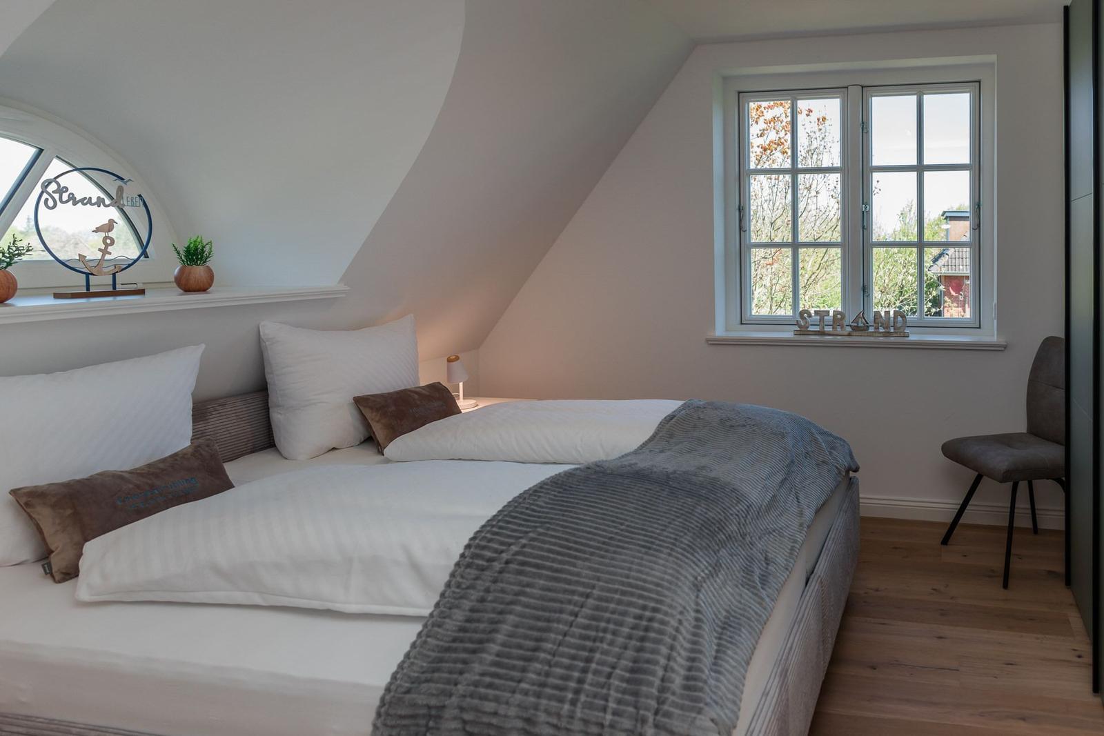 Bedroom with double bed, window, and wooden floor. Decor with beach motifs.