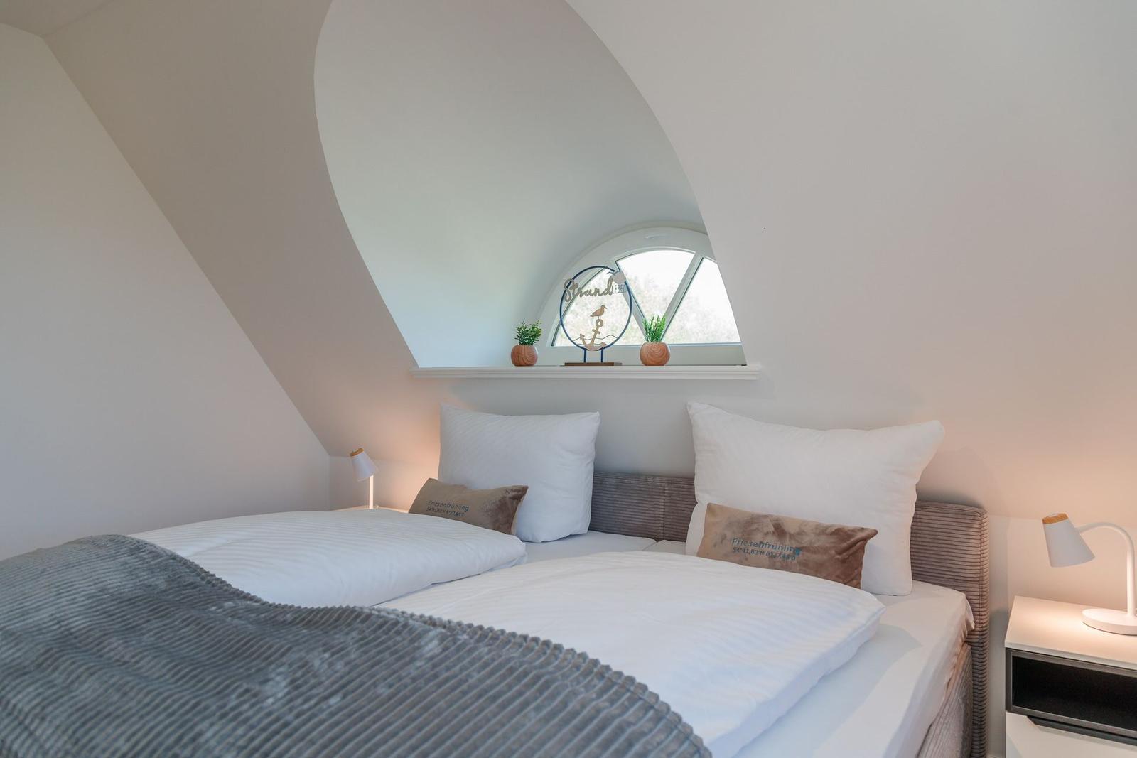 Bedroom with sloped ceiling, bed, nightstand, and window with decoration.