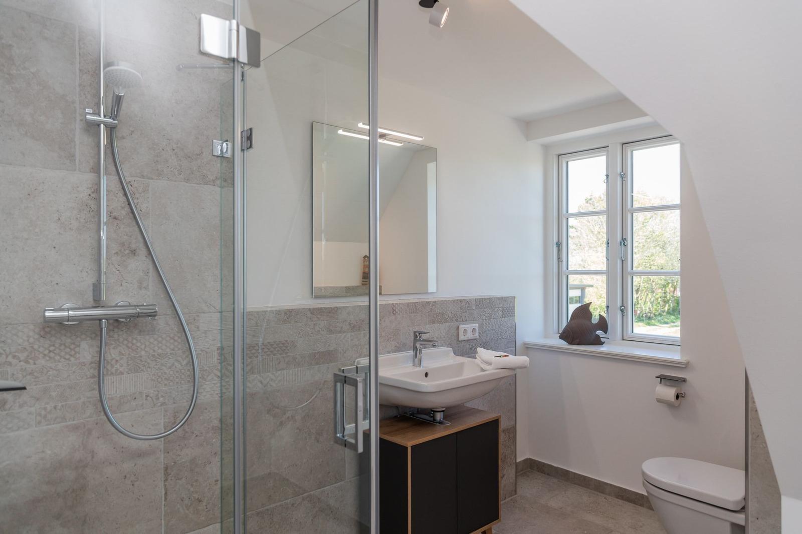 Bathroom with shower, sink, and toilet. Window with view outside.
