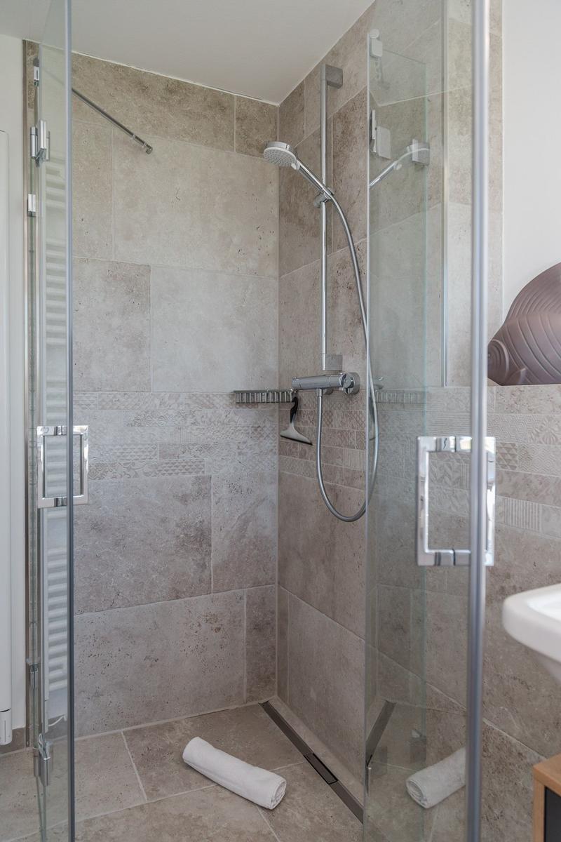 Shower cabin with glass door, stone tiles, and handheld shower