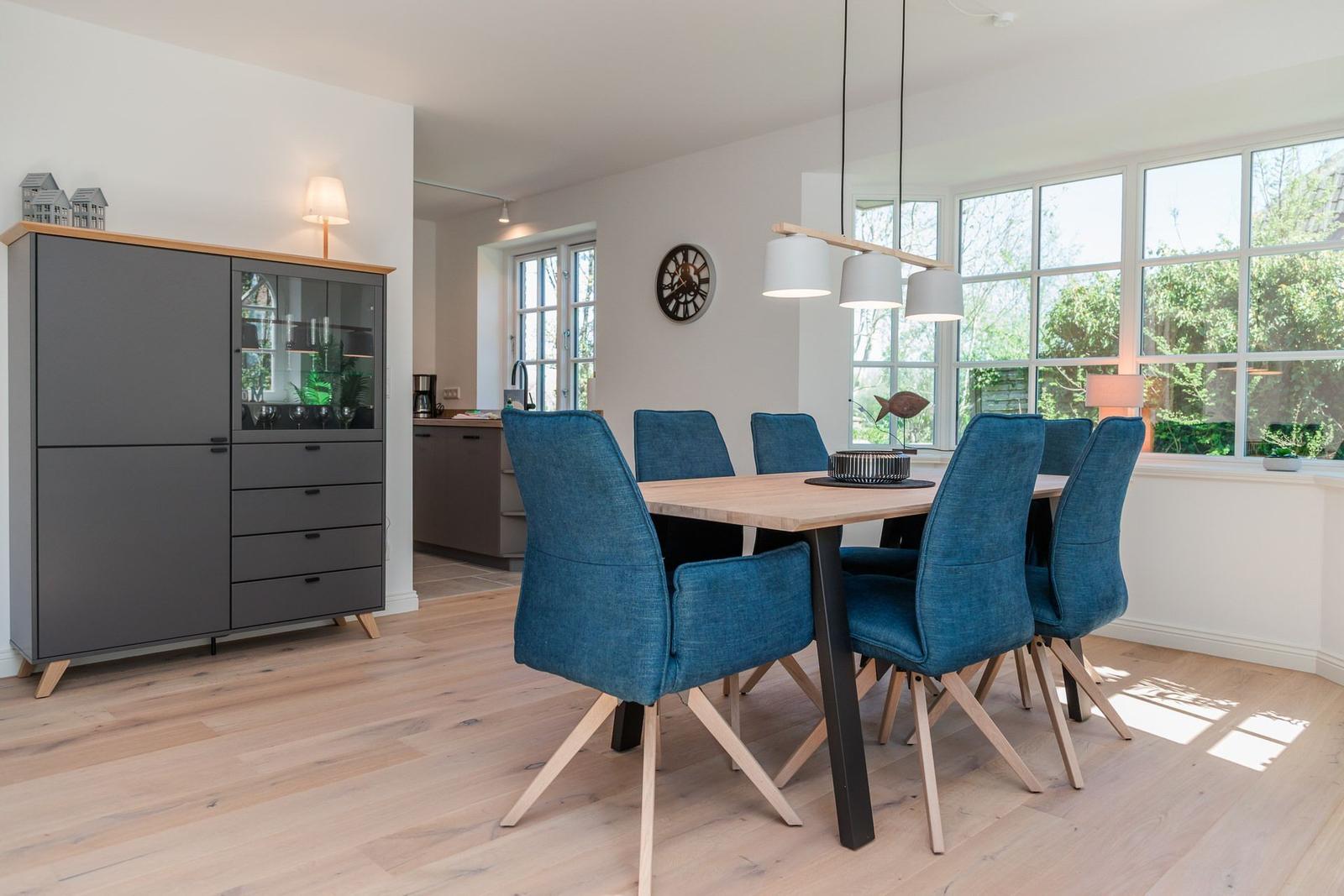 Dining room with blue chairs and wooden table. Large windows and gray sideboard.