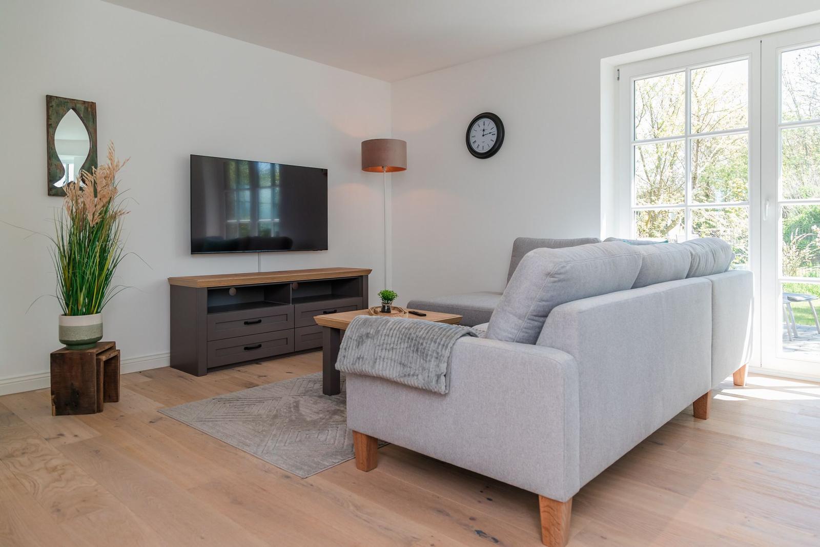 Wohnzimmer mit Sofa, Fernseher und Holzboden. Durchgangstür führt nach draußen.