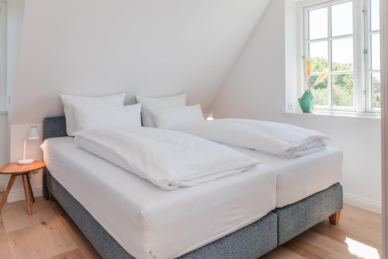 Schlafzimmer mit Doppelbett, Fenster und Nachttisch.