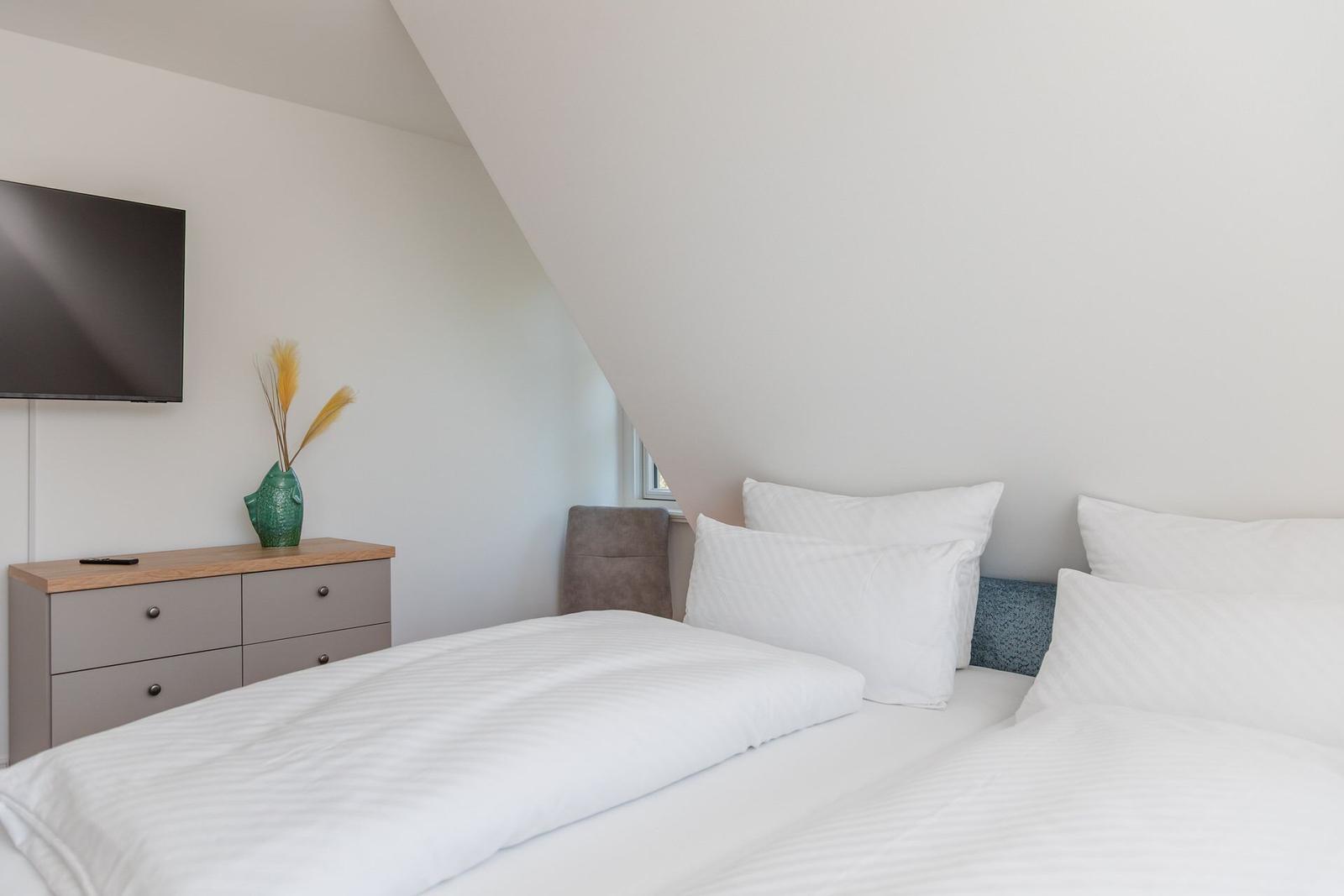 Schlafzimmer mit Doppelbett, Schrank und Wandfernseher unter schräger Decke.
