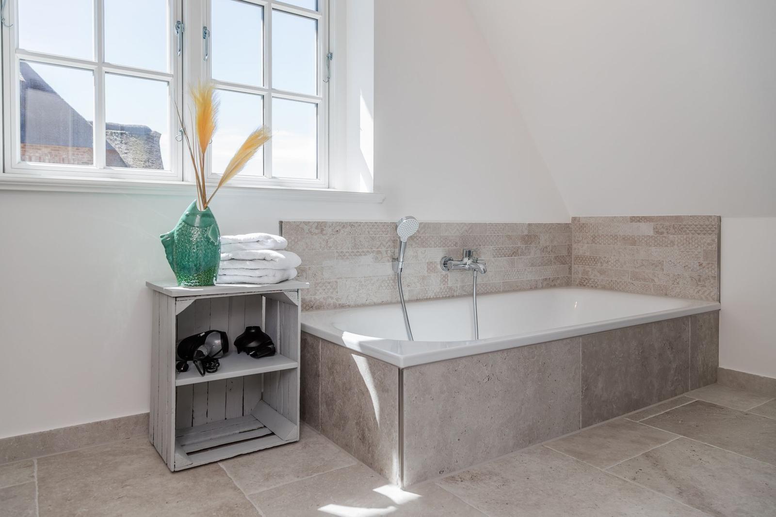 Bad mit Badewanne, Fenster und Holzregal mit Handtuch und Vasen.