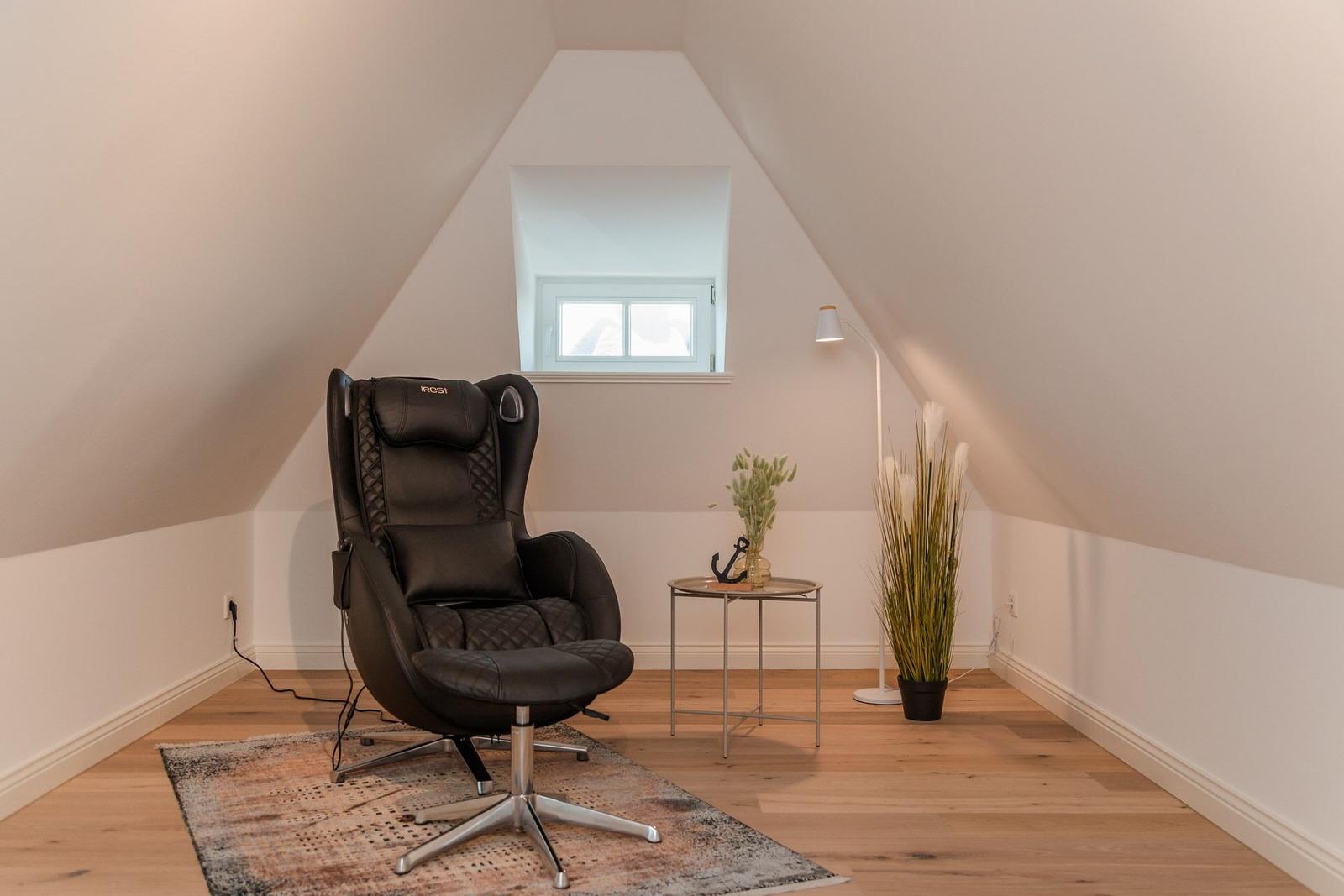Schwarzer Sessel mit Fußstütze, kleiner Tisch und Pflanzen in einem Dachzimmer mit Holzboden und Fenster.