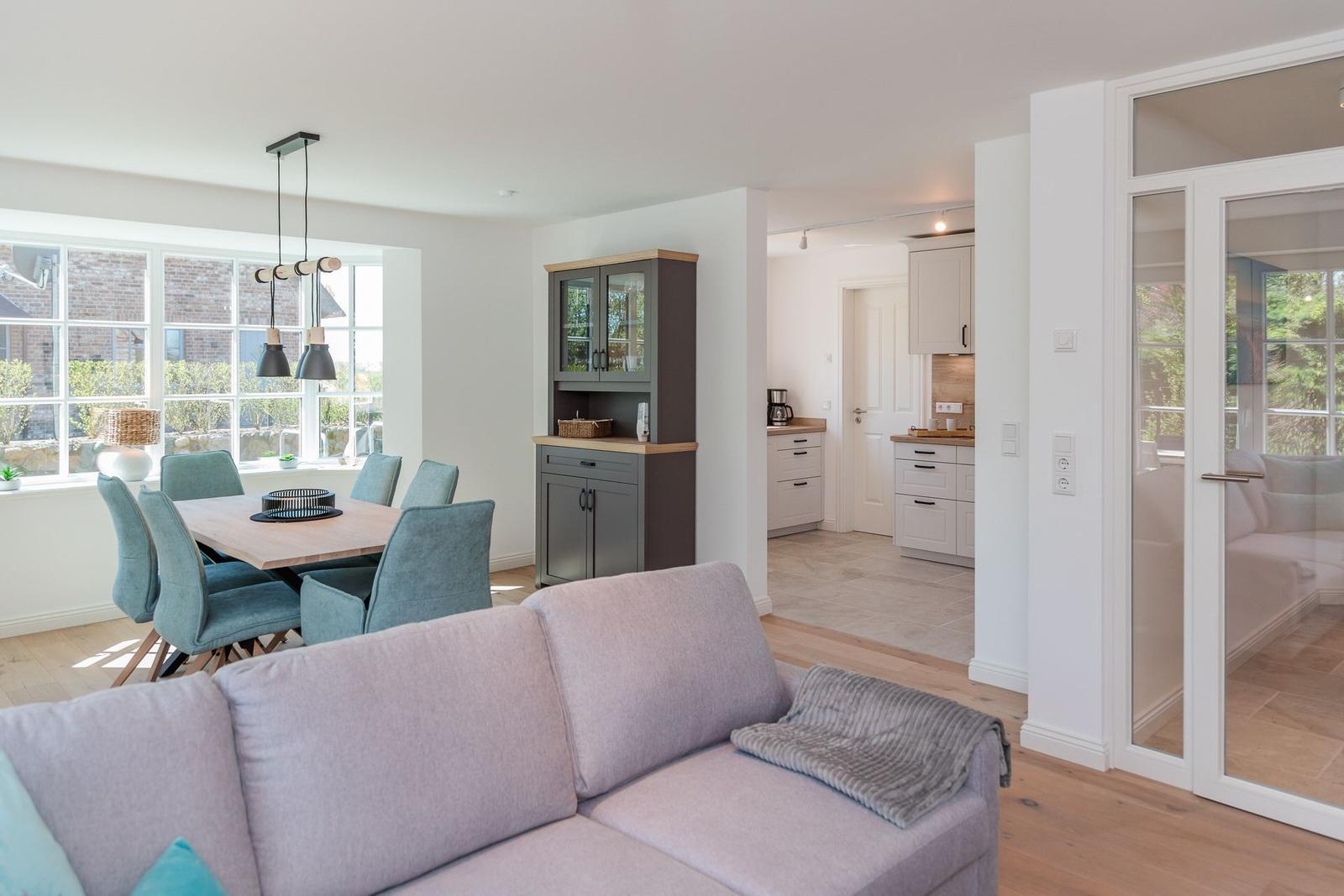 Wohn- und Essbereich mit Sofa, Tisch und Stühlen. Küche und Schlafzimmer sind angebaut.