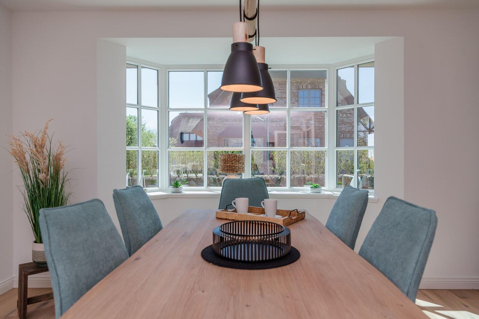 Esszimmer mit Holztisch, blauen Stühlen und großem Fensterblick.