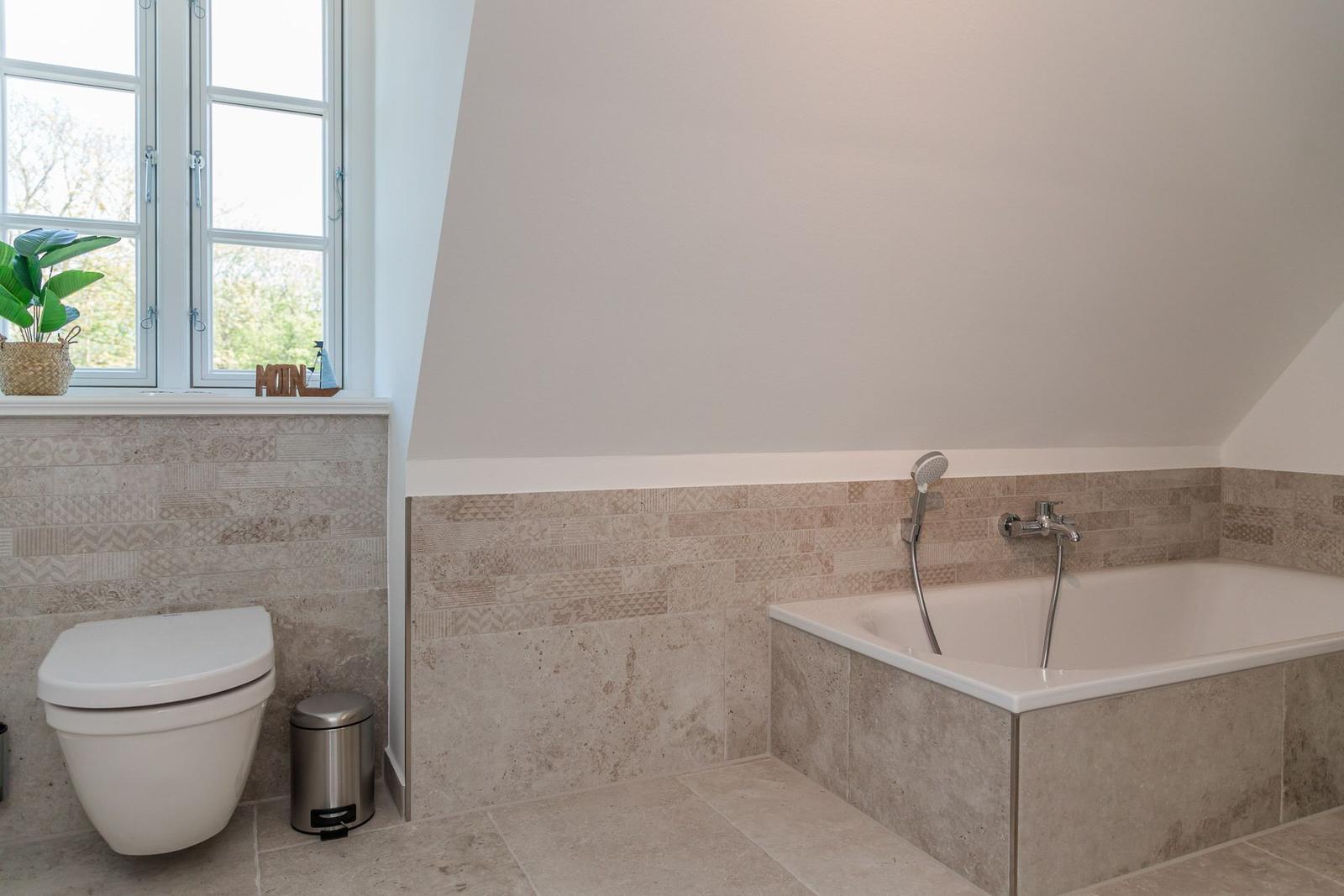 Bad mit Badewanne, Toilette und Fenster mit Pflanze.