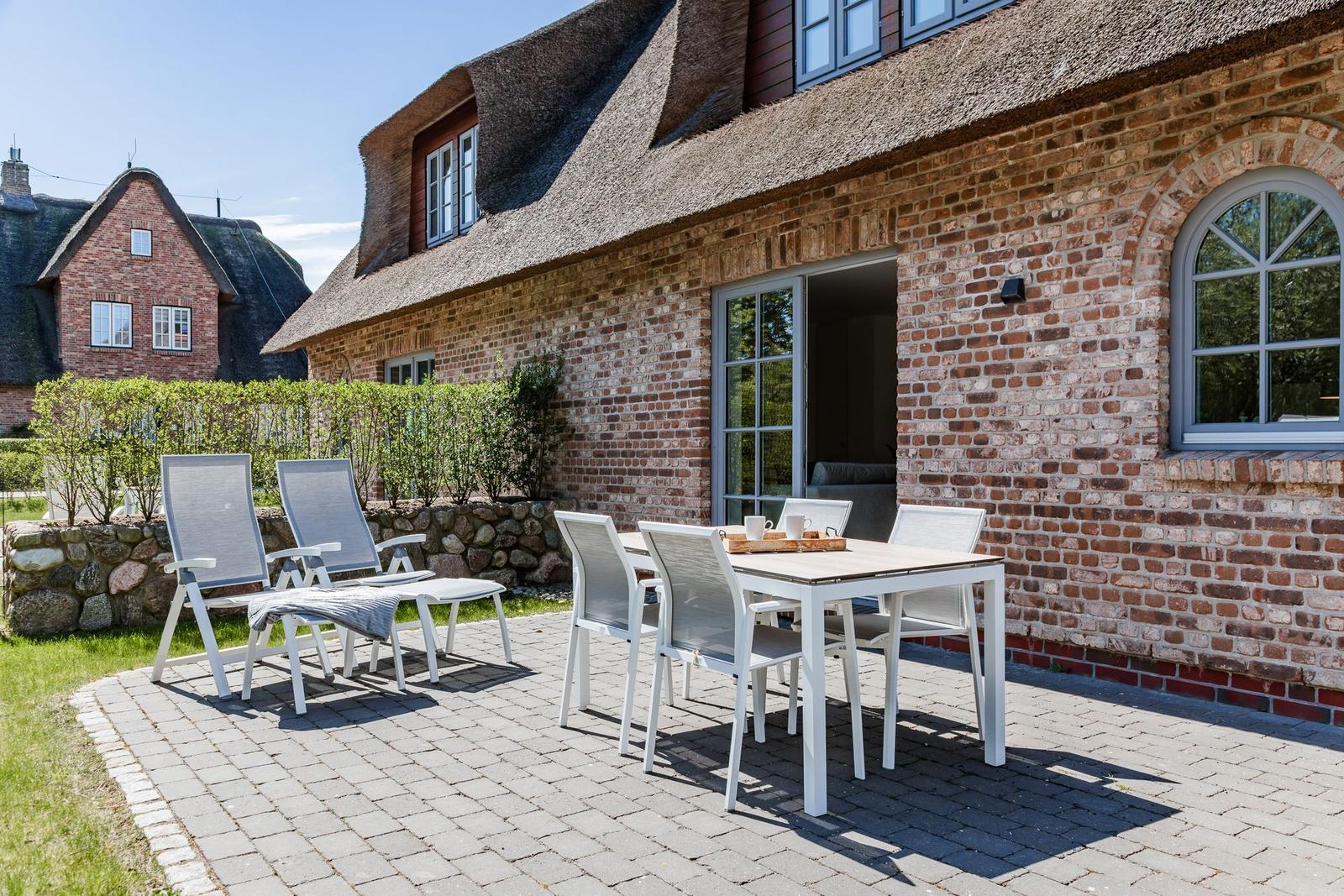 Terrasse mit Tisch, Stühlen und Liegestühlen vor einem Backsteinhaus mit Strohdach.