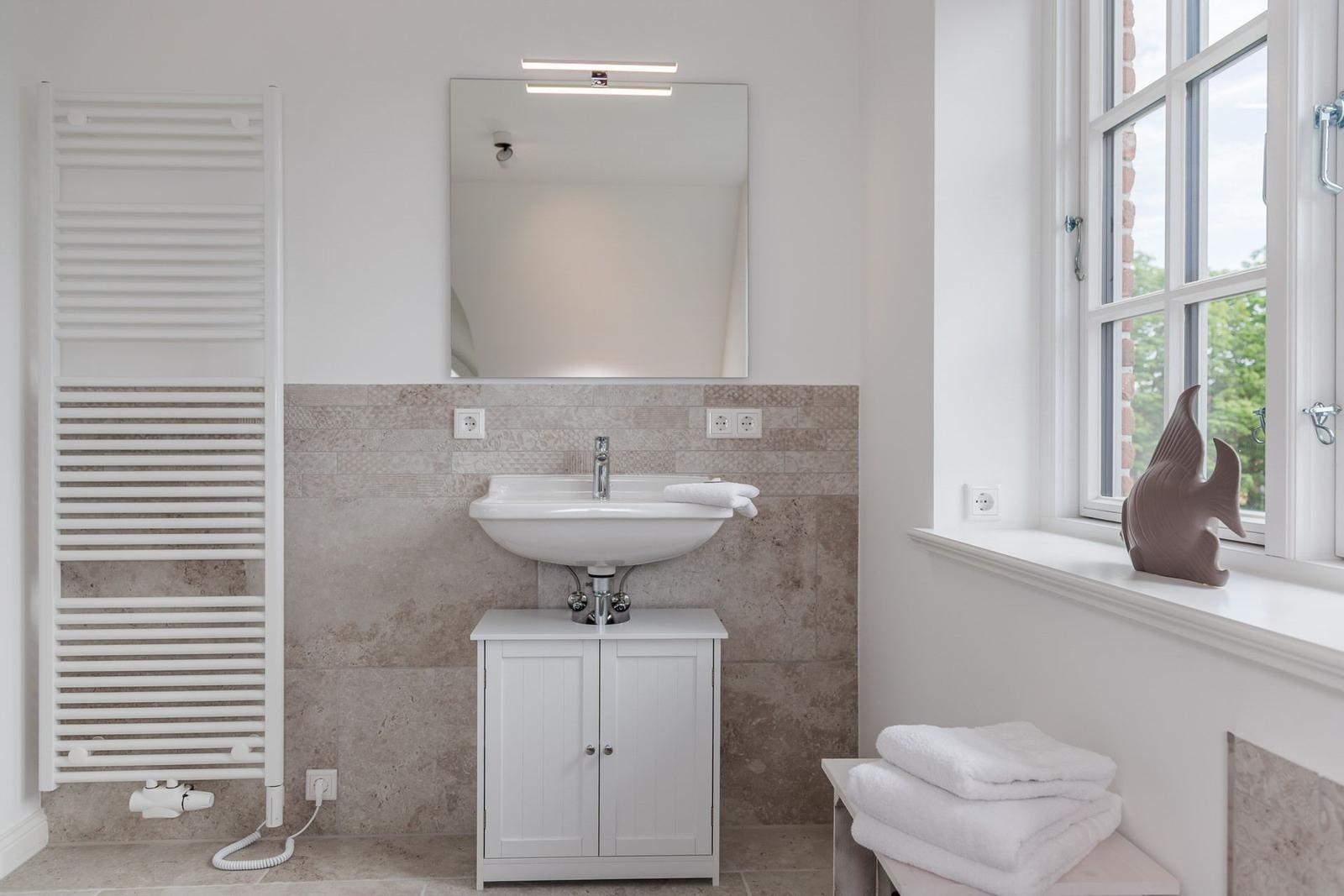 Badezimmer mit Waschbecken, Spiegel und Fenster. Weiße Heizung und Handtücher.