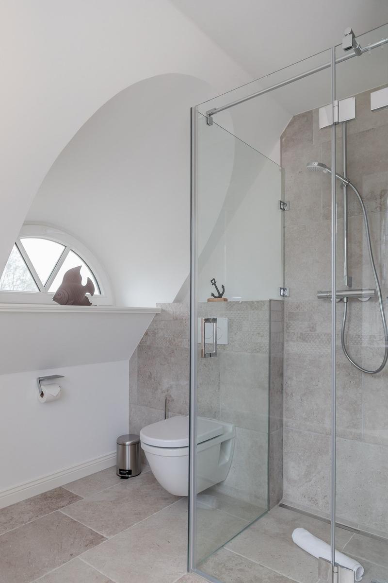 Badezimmer mit Dusche, Toilette und Fenster unter einem Bogen