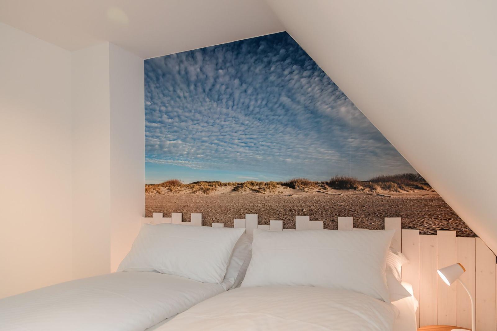 Schlafzimmer mit Dachschrägen und Strandbild an der Wand.