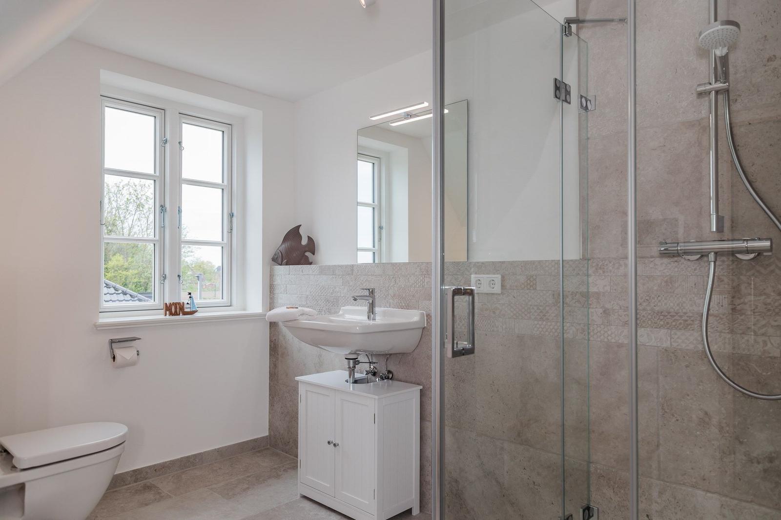 Badezimmer mit Dusche, Waschbecken und Toilette. Fenster mit Blick auf Außenbereich.