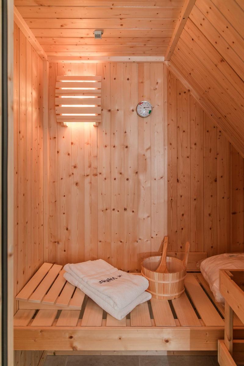 Sauna mit Holzbank, Korb und Handtuch. Wanduhr und Heizung sichtbar.