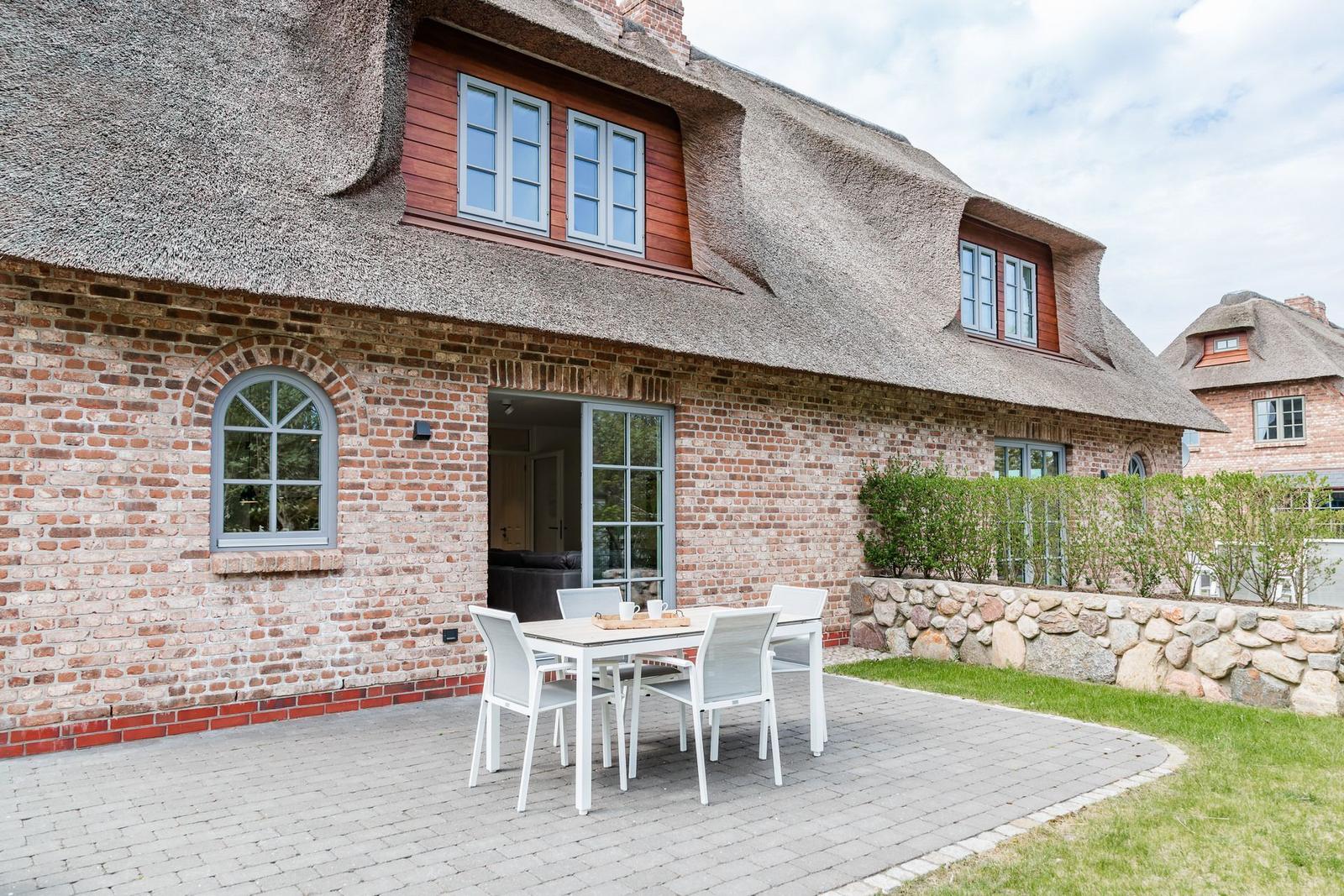 Haus mit Strohdach, Backsteinmauer und Terrasse mit weißem Tisch und Stühlen.