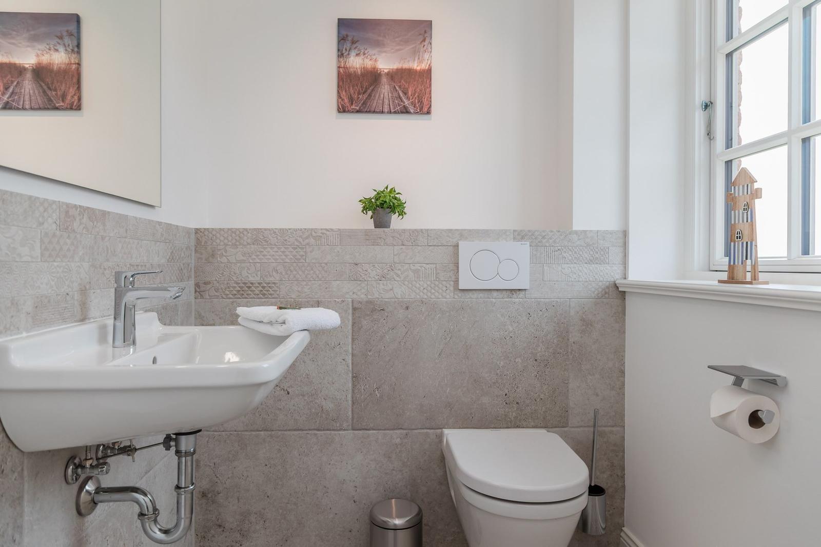 Badezimmer mit Waschbecken, Toilette und Fenster. Wand mit Mosaikfliesen und Bildern.