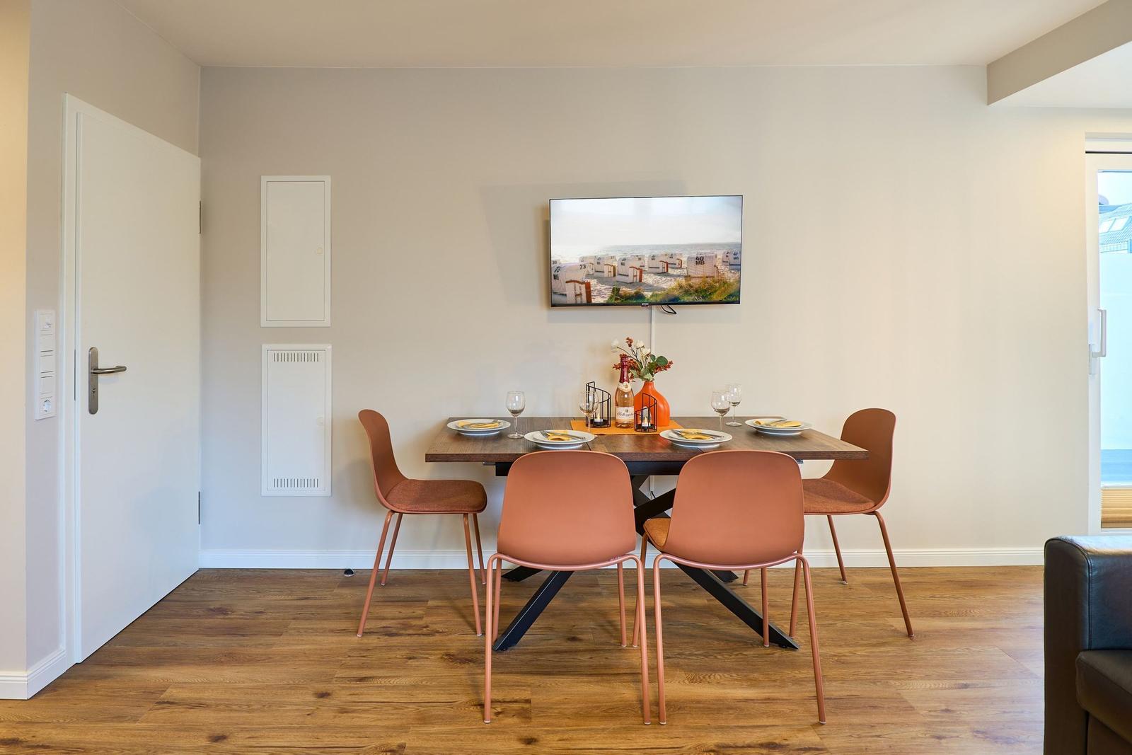 Essbereich mit Tisch, vier Stühlen und Wandbild. Holzboden und weiße Wände.