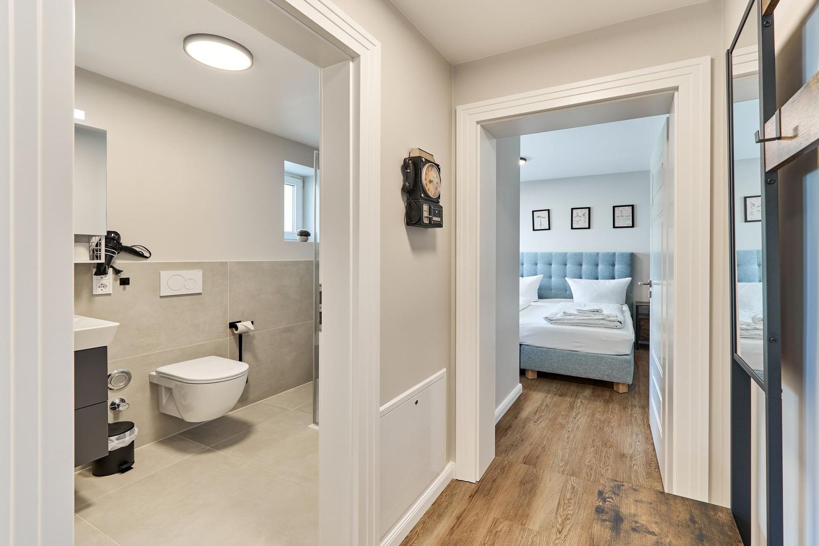 Badezimmer mit Toilette und Spiegel. Schlafzimmer mit Bett und Wandbildern.