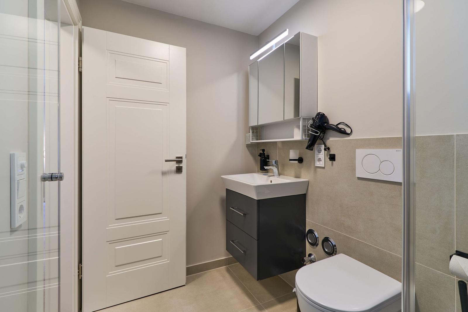 Badezimmer mit Waschbecken, Spiegelschrank und Toilette. Dusche mit Glaswand.