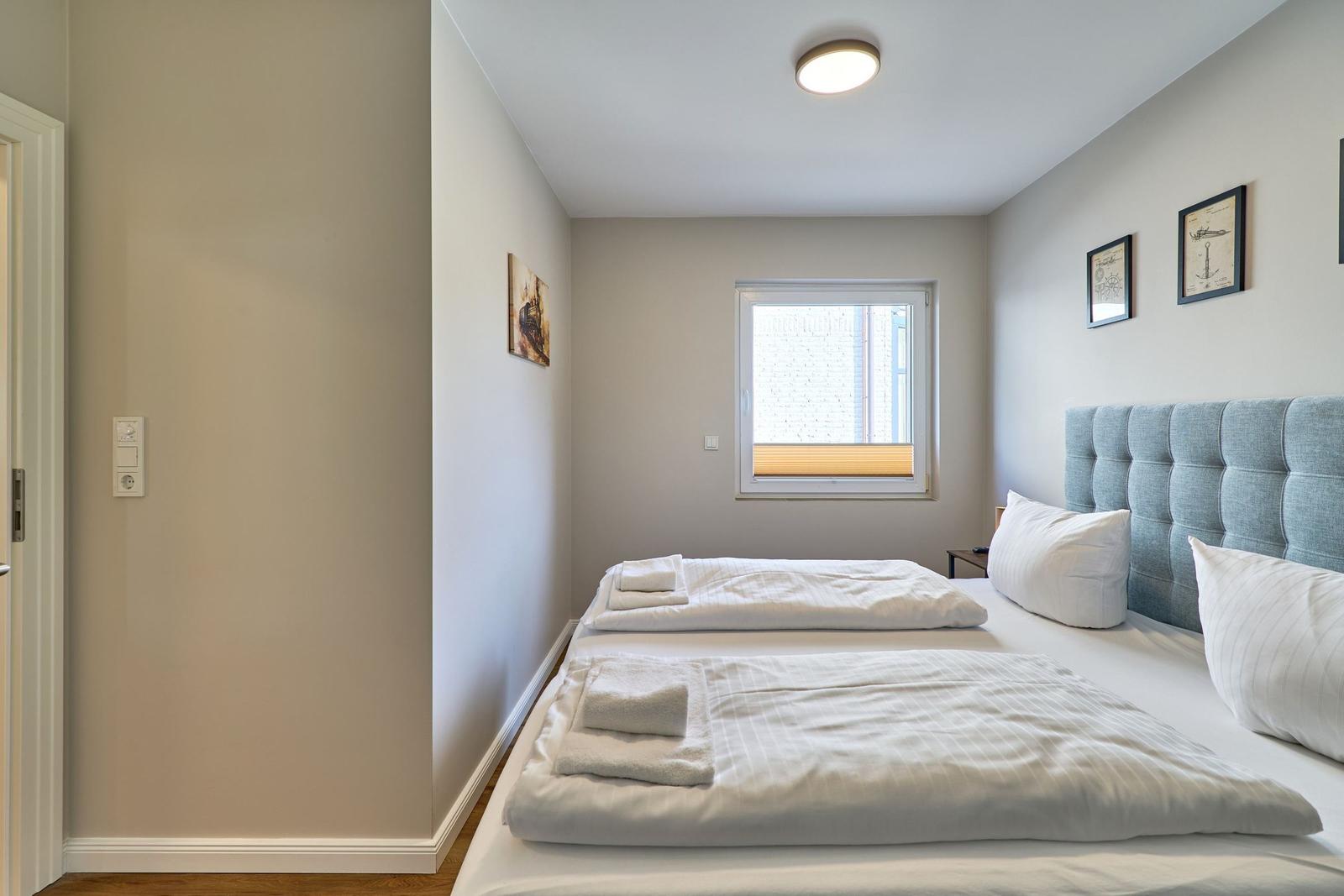 Schlafzimmer mit Doppelbett, Fenster und Wandbildern.