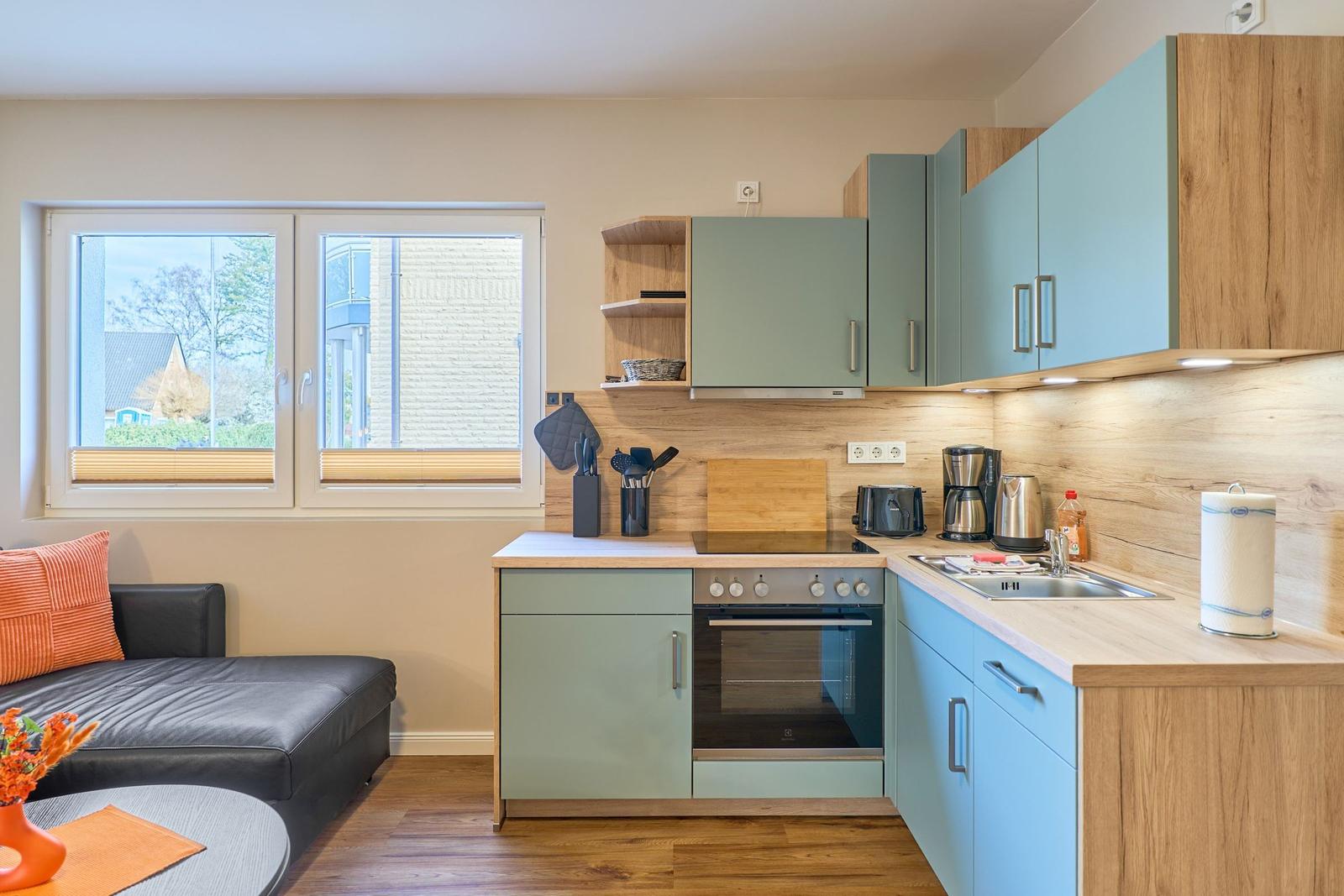 Küche mit Holzoberflächen und hellblauen Schränken. Fenster, Sofa und Arbeitsfläche sind sichtbar.